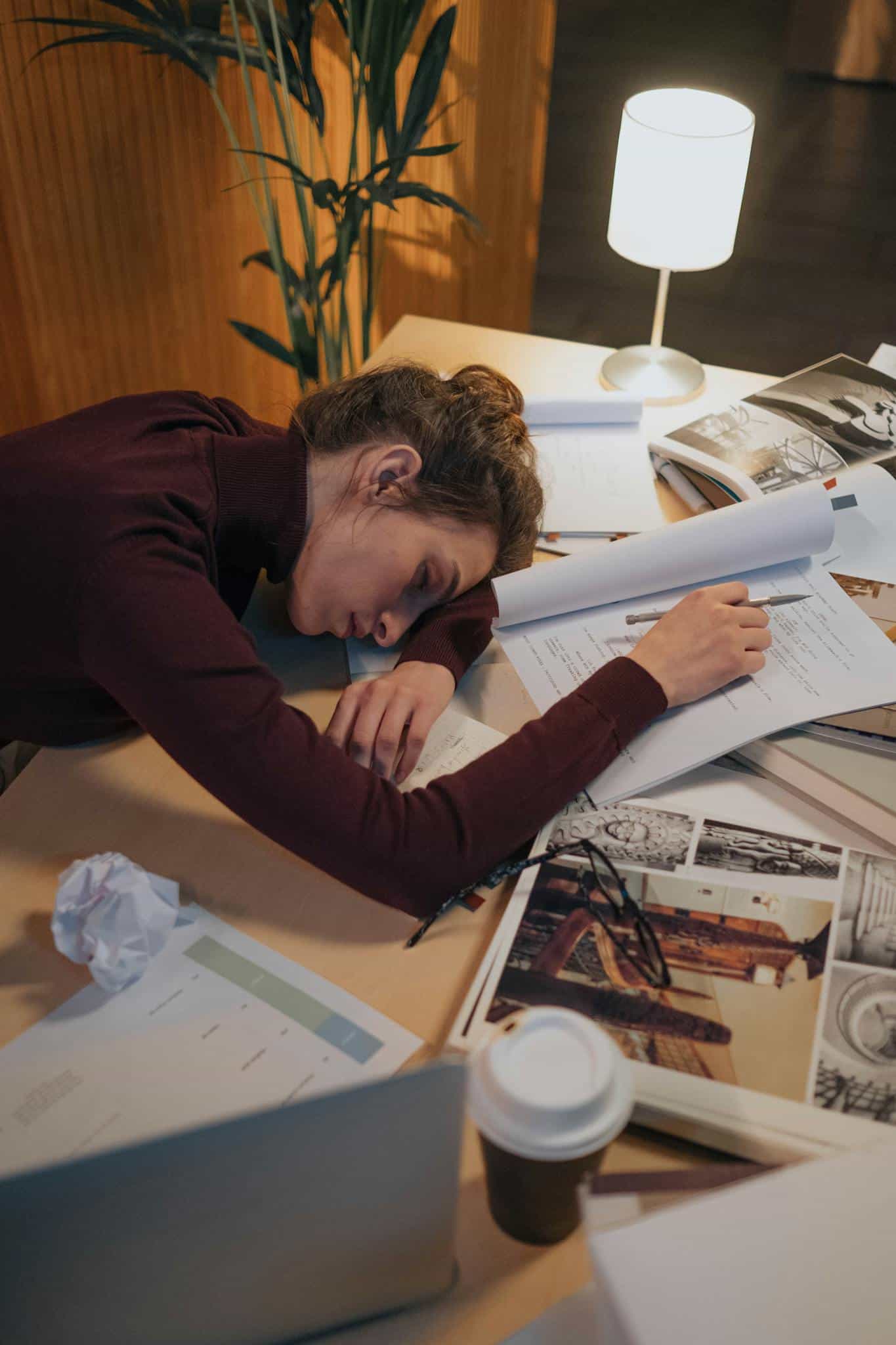 Exhausted woman sleeping on her desk filled with papers and laptop, illustrating work fatigue.