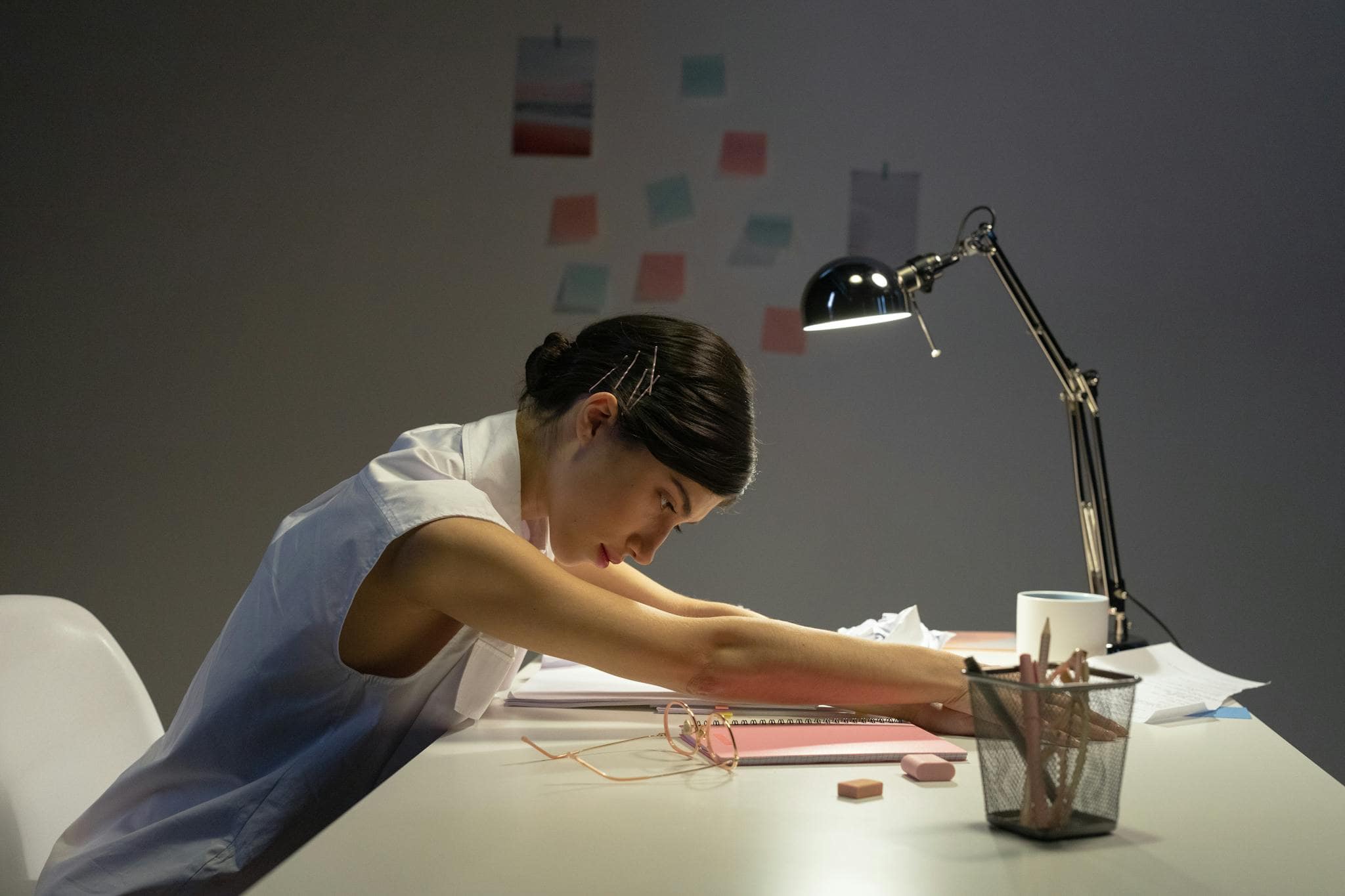 Tired young woman resting at her desk in a dimly lit office environment.