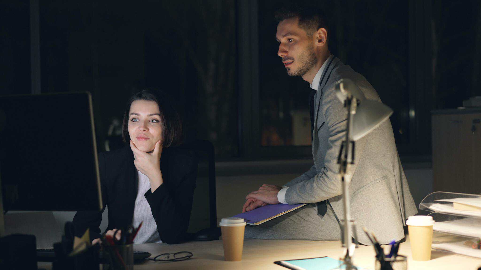 Two professionals collaborating at an office desk during the night. Focused teamwork.